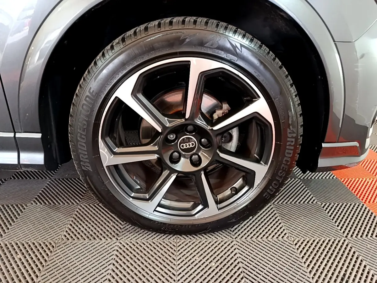 Gros plan sur la roue avant droite d’un Audi Q3 gris foncé, avec jante alliage à cinq branches doubles.