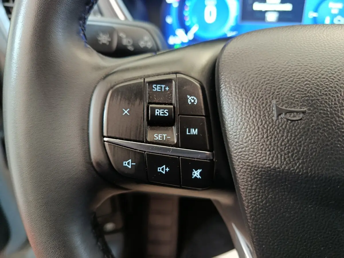 Gros plan sur les commandes du régulateur de vitesse au volant cuir noir du Ford Kuga gris foncé 2023.