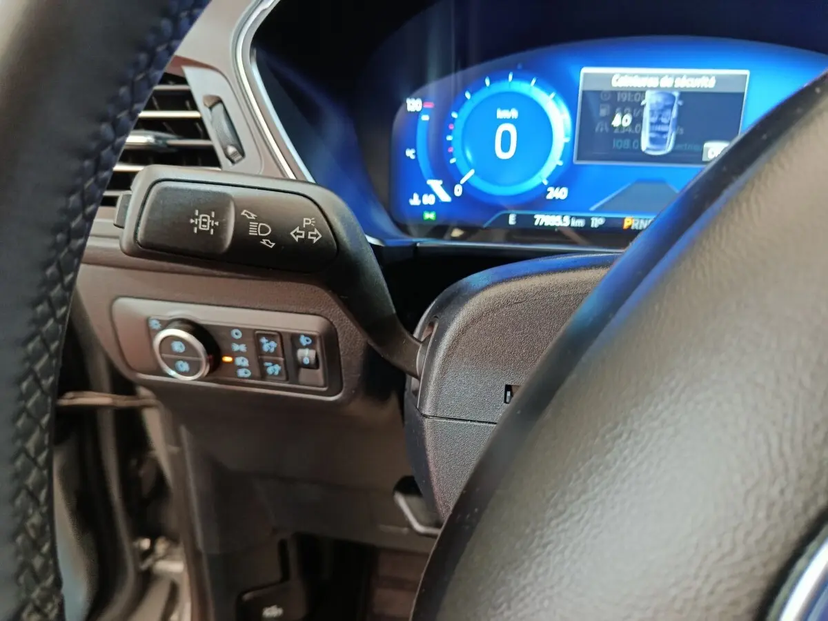 Gros plan sur le volant et le combiné d'instruments numérique bleu du Ford Kuga 2023, version hybride.