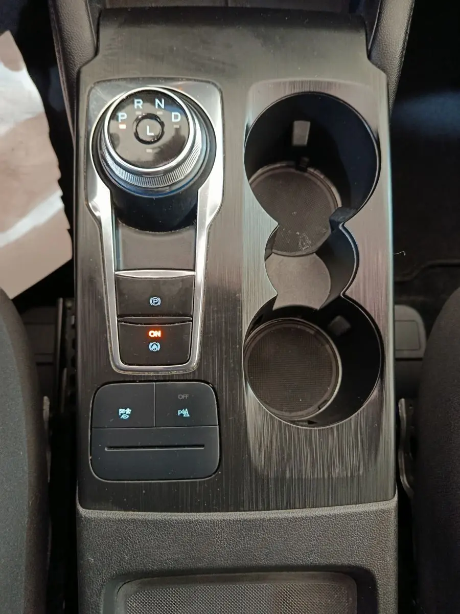 Vue plongeante sur la console centrale noire du Ford Kuga 2023 avec molette de boîte auto et porte-gobelets.