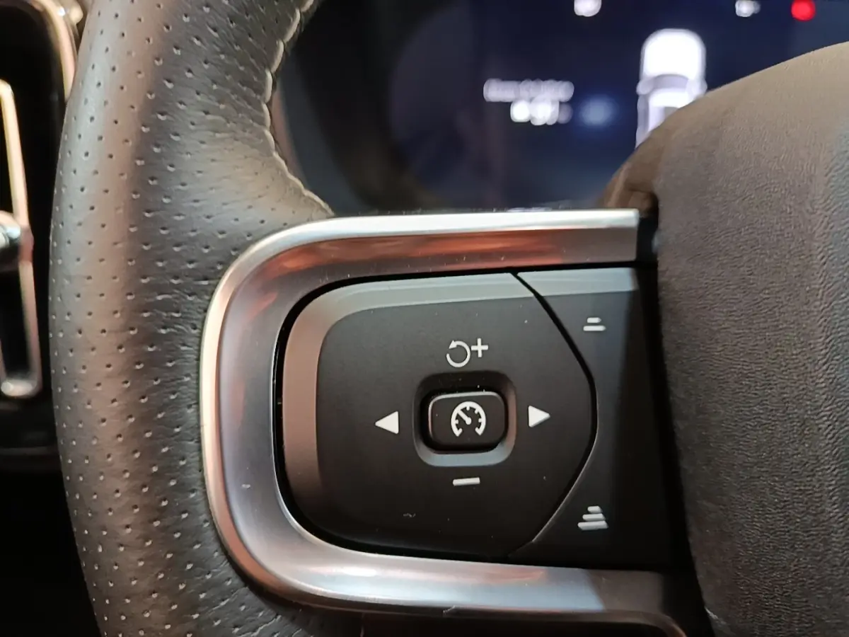 Gros plan sur les commandes de régulateur de vitesse au volant cuir perforé gris clair du Volvo XC40 électrique P8 R-Design.