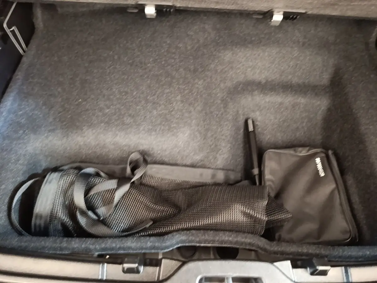 Coffre ouvert d’un Volvo XC40 gris clair, vue plongeante sur le rangement avec filet et sac noir.