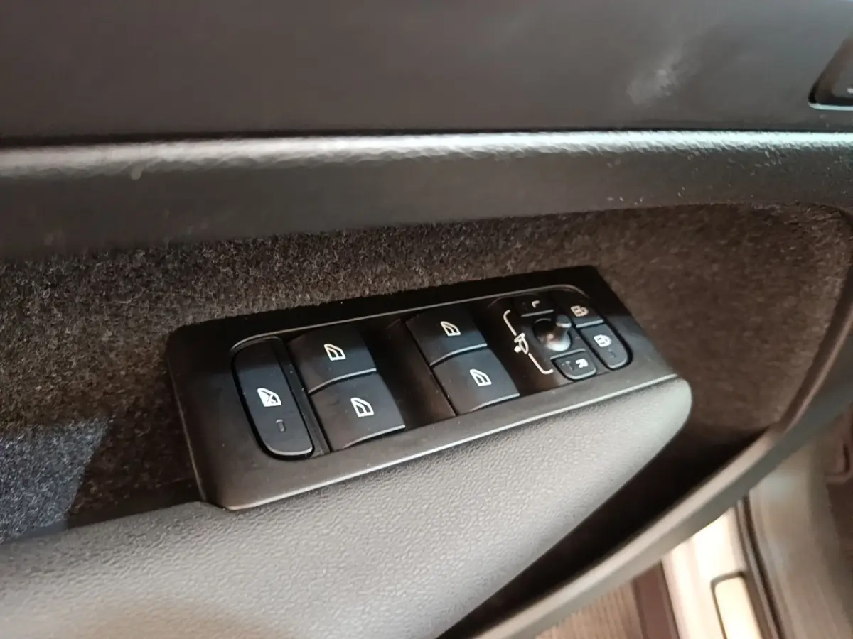 Gros plan sur les commandes de lève-vitres et rétroviseurs côté conducteur du Volvo XC40 gris clair électrique.