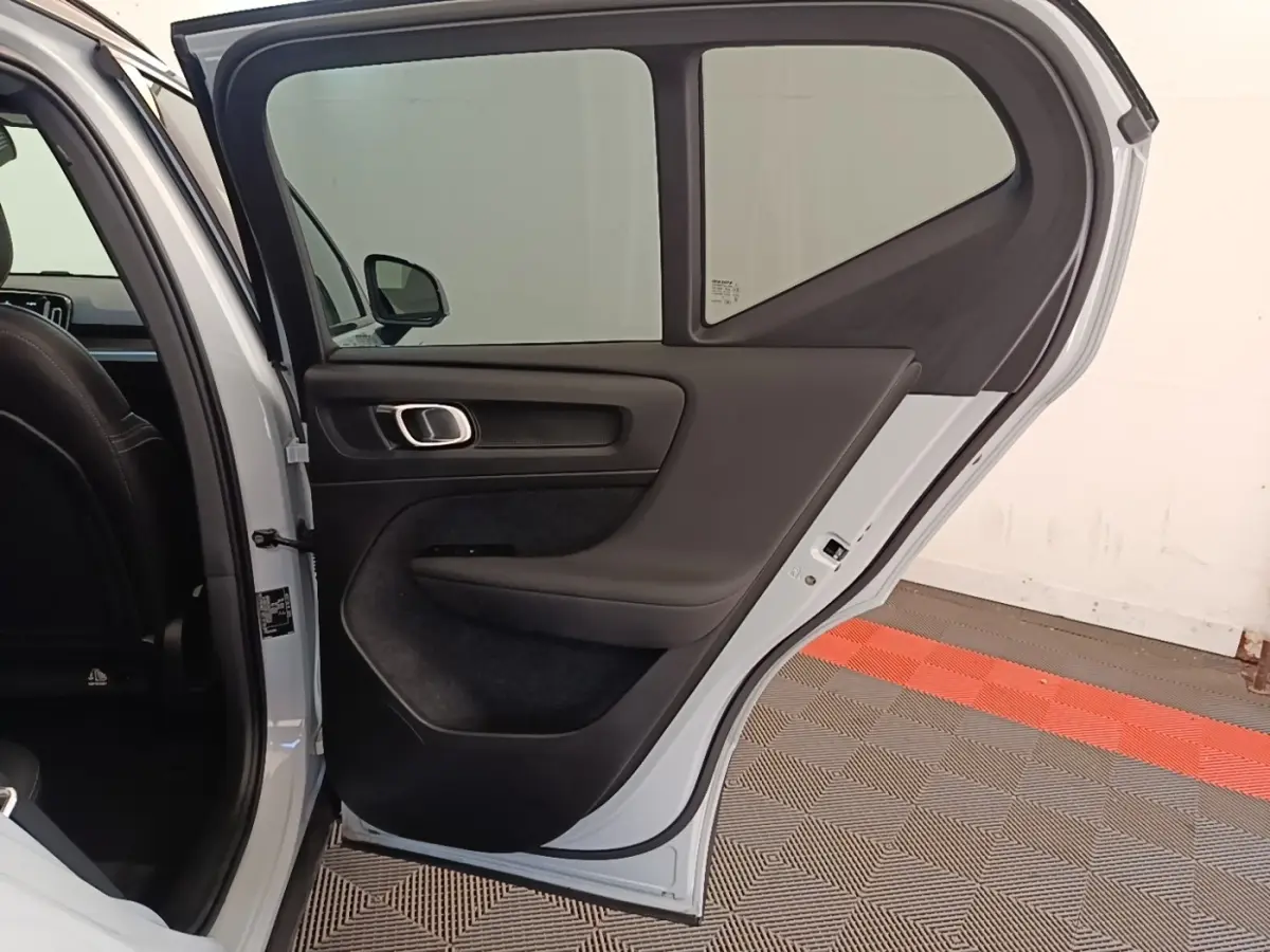 Vue intérieure de la porte arrière gauche ouverte d’un Volvo XC40 gris clair, avec garniture noire et poignée argentée.
