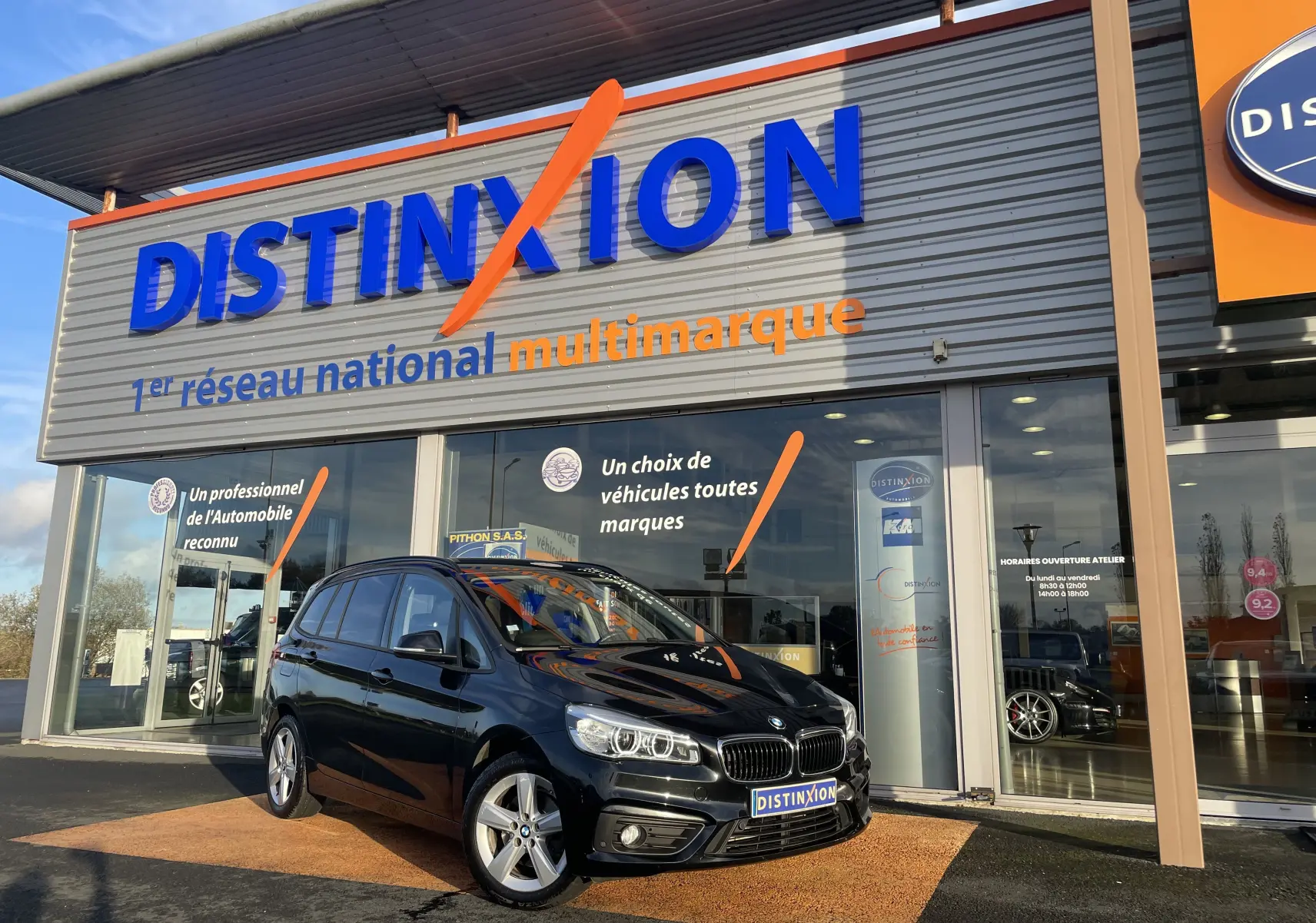 BMW Série 2 Gran Tourer noire vue en 3/4 avant droit devant un showroom Distinxion multimarque.