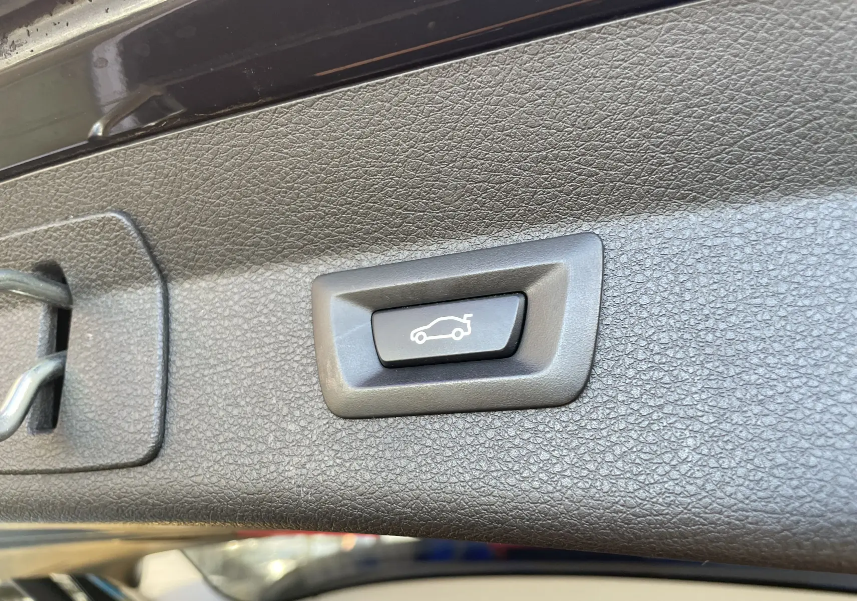 Bouton d'ouverture électrique du hayon sur le bord intérieur noir du coffre d'une BMW Série 2 Gran Tourer F46 noire.