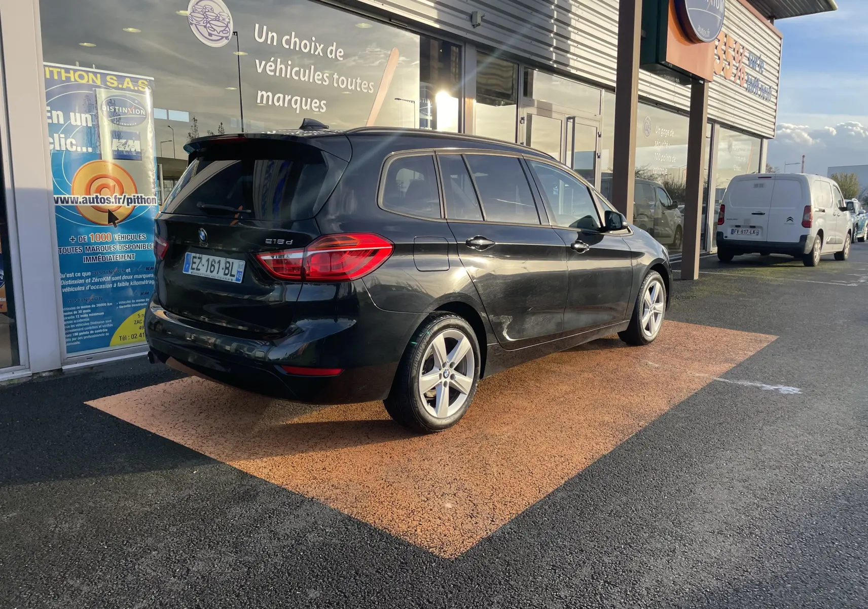 BMW Série 2 Gran Tourer noire vue en 3/4 arrière côté gauche, garée devant une concession automobile.