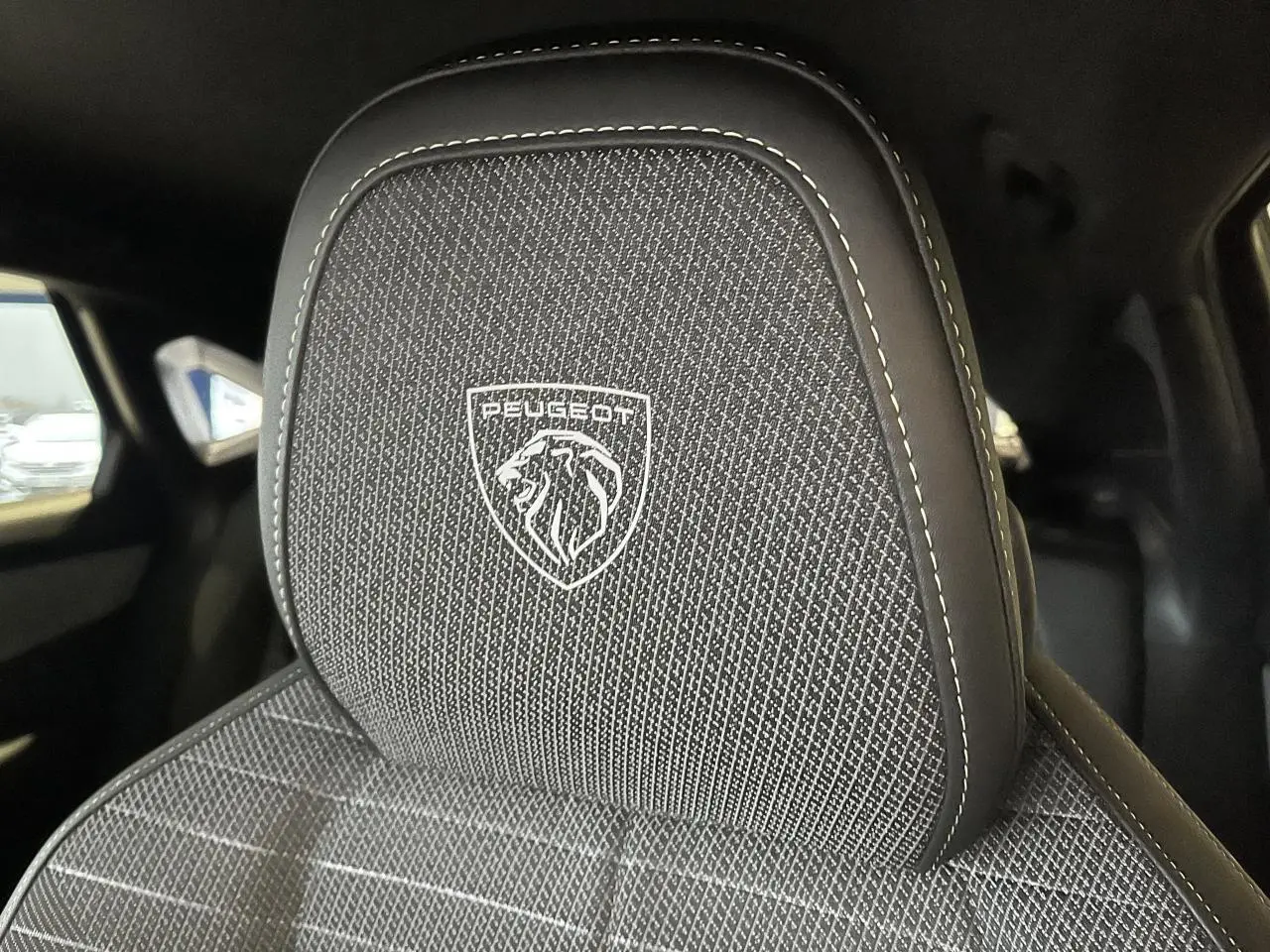 Gros plan sur l'appui-tête avant avec logo Peugeot brodé sur la sellerie tissu du Peugeot 3008 gris titanium.