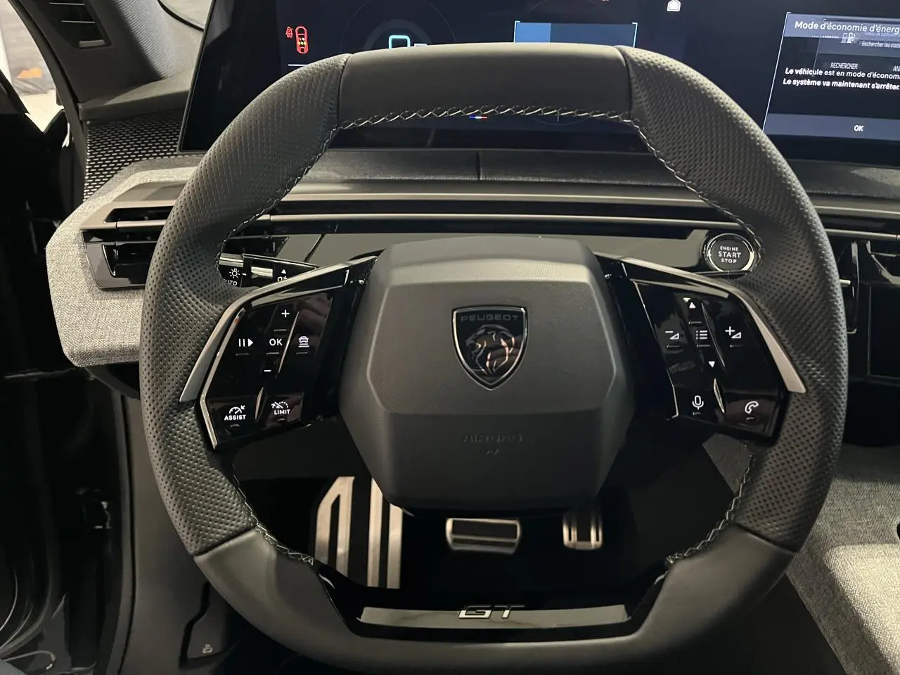 Vue rapprochée du volant compact noir perforé avec logo Peugeot et badge GT du Peugeot 3008 gris titanium 2025.