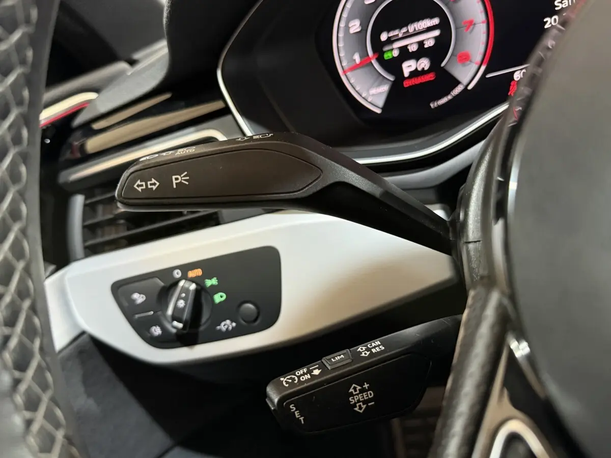 Gros plan sur la commande de clignotants et le tableau de bord numérique de l’Audi A4 gris foncé, côté gauche du volant.