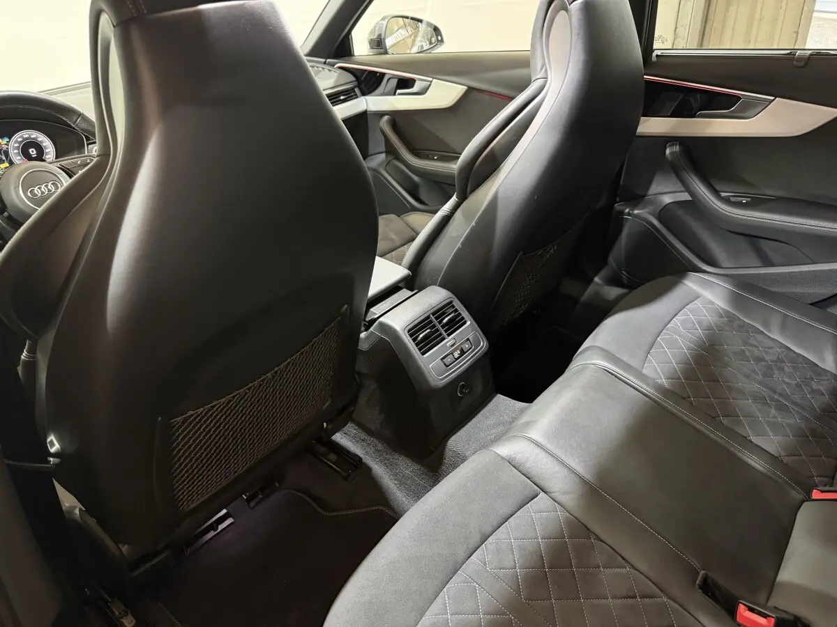 Vue intérieure arrière de l'Audi A4 gris foncé, montrant les sièges en cuir et la console centrale avec ventilation.
