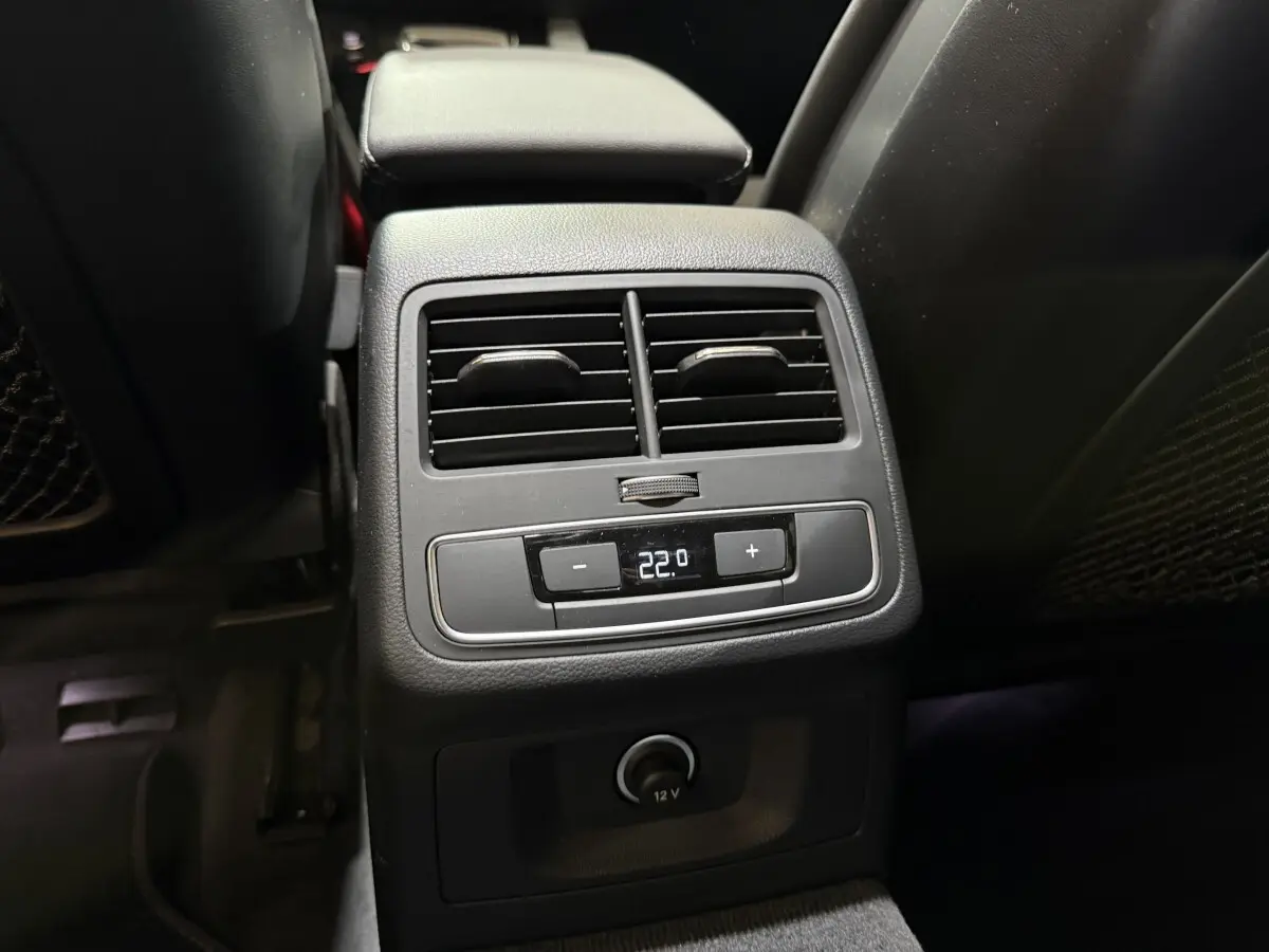 Vue rapprochée de la console arrière noire avec commandes climatisation et prise 12V dans l’Audi A4 gris foncé 2022.