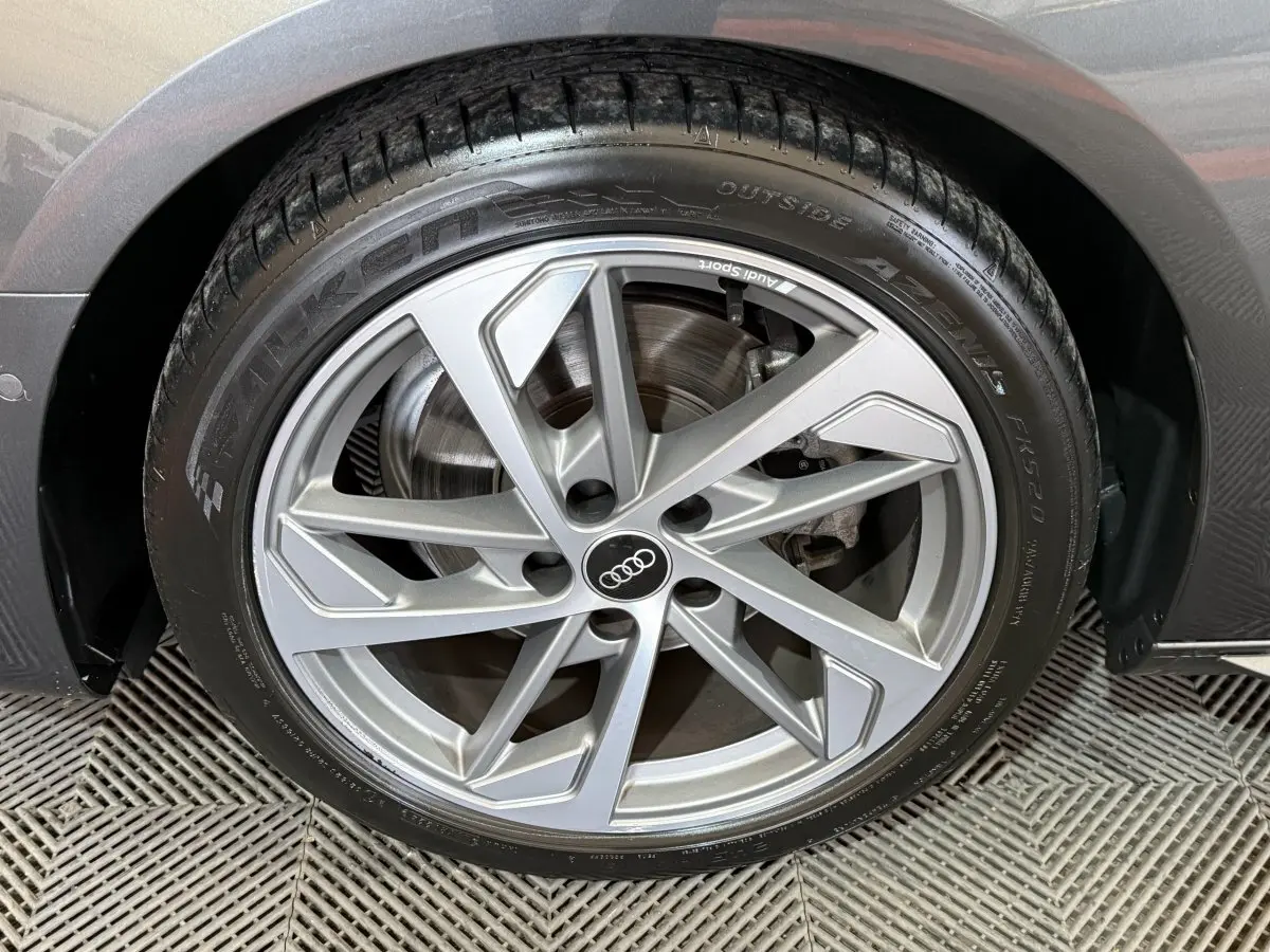 Gros plan sur la jante alliage argentée de l'Audi A4 gris foncé, montrant le logo Audi au centre.