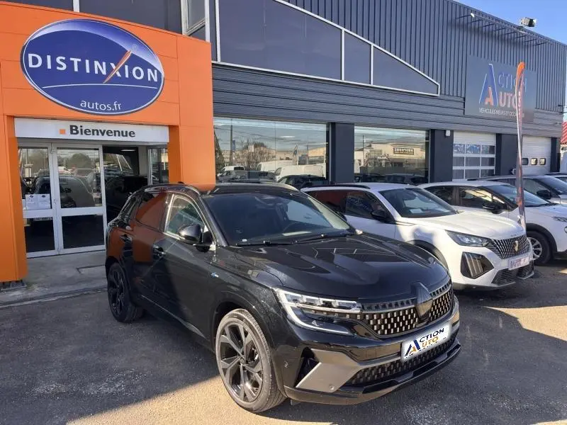 Vue 3/4 avant droite d'un Renault Austral noir étoilé avec jantes alu, stationné devant un garage automobile.