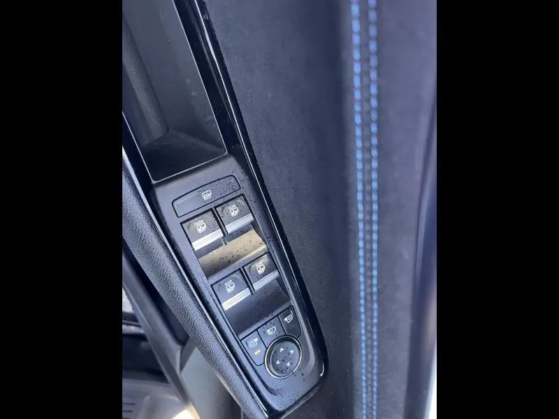 Gros plan sur les commandes des vitres et rétroviseurs côté conducteur du Renault Austral noir étoilé avec surpiqûres bleues.