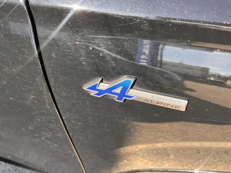 Gros plan sur l'emblème bleu A4 Esprit Alpine sur la porte noire étoilée d'un Renault Austral 2023.