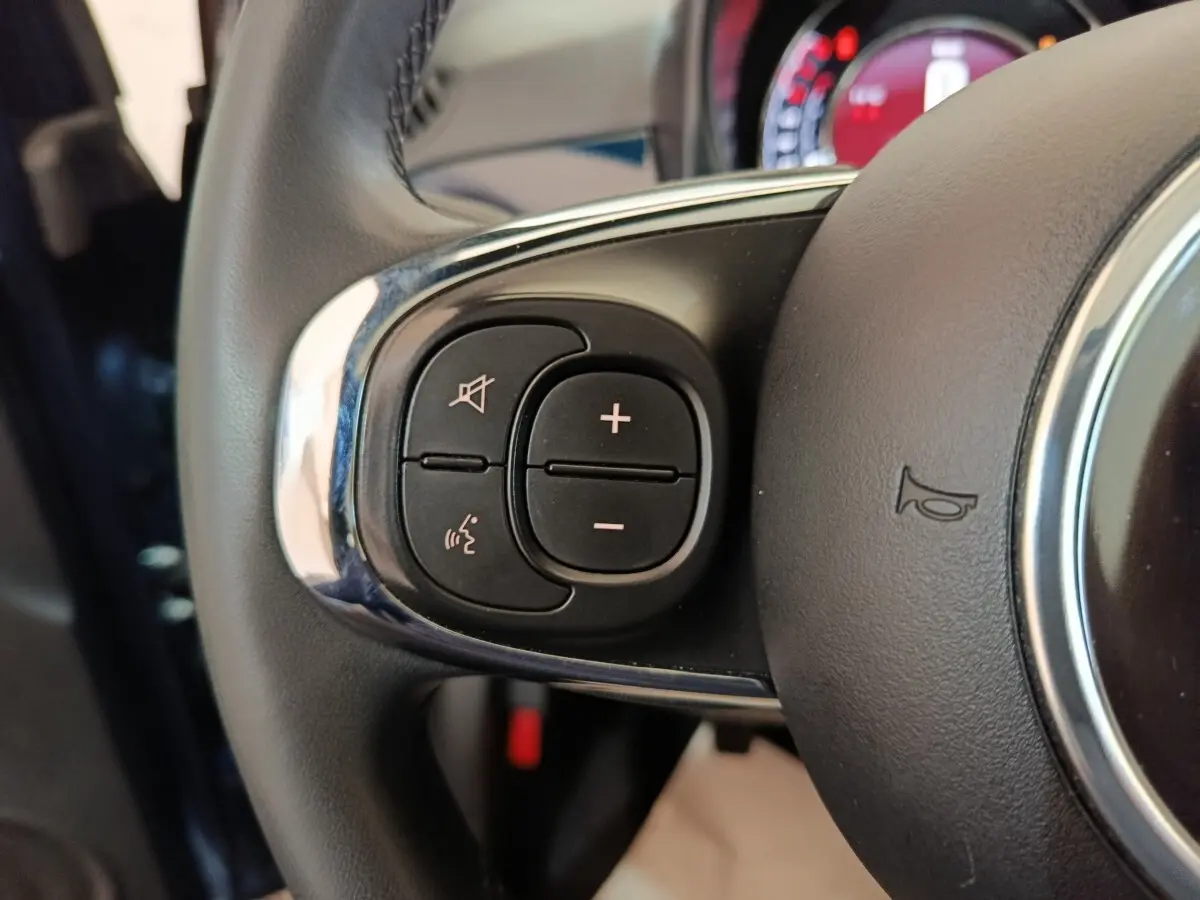 Gros plan sur les commandes du volant cuir de la FIAT 500 Hybrid bleu, avec boutons de volume et reconnaissance vocale.