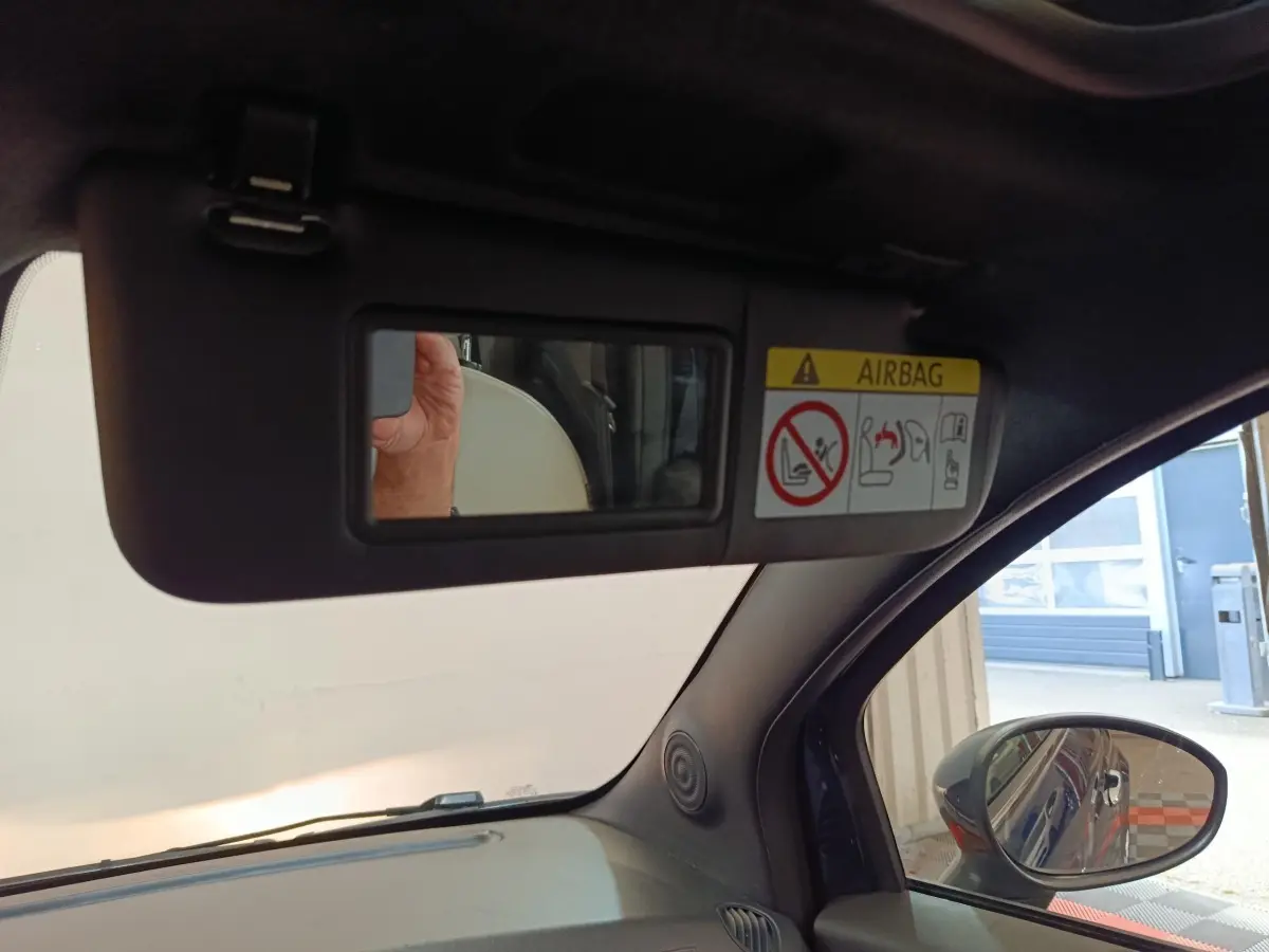 Vue intérieure côté conducteur du pare-soleil avec miroir et avertissement airbag, rétroviseur extérieur bleu visible.
