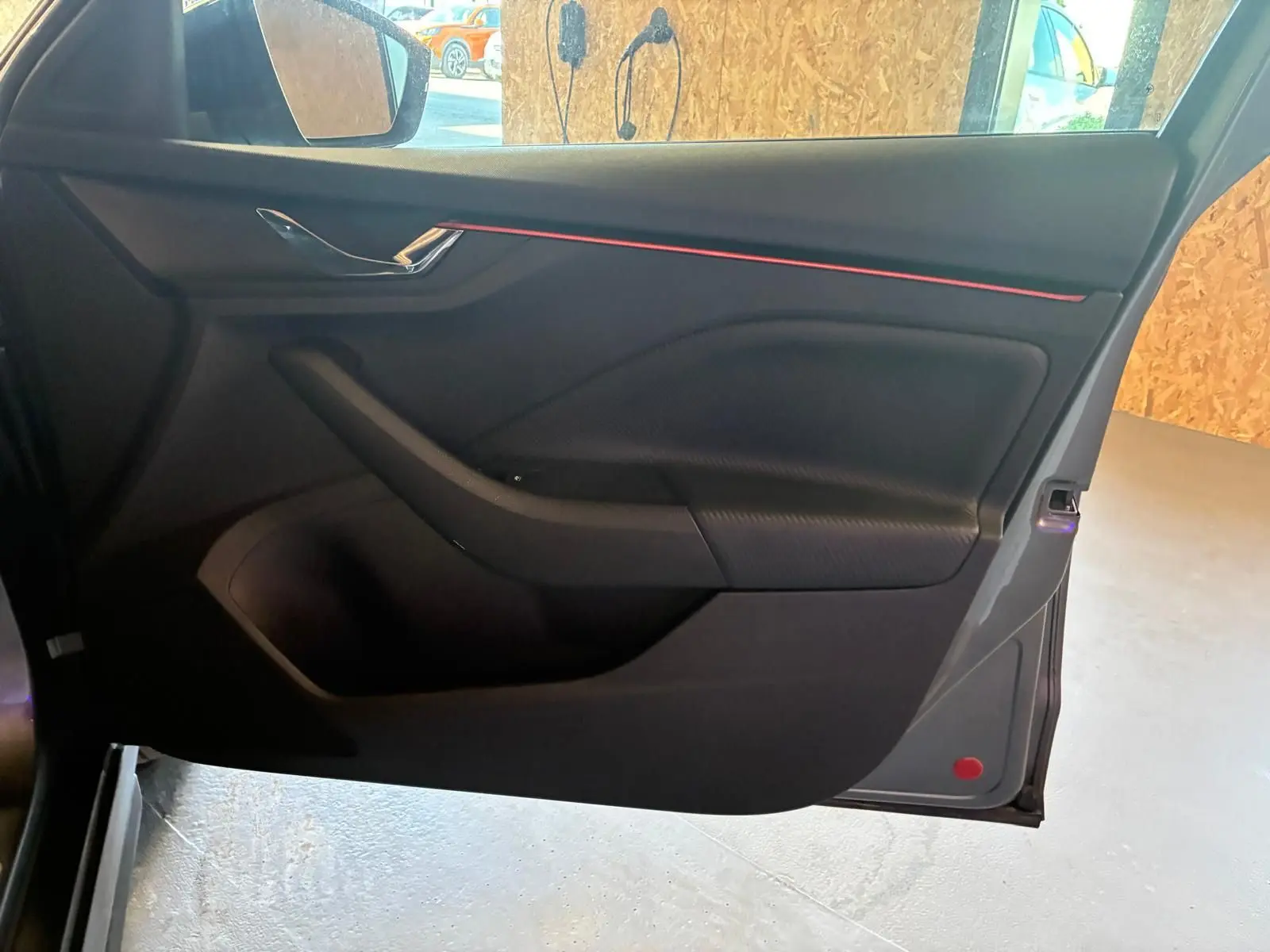 Vue intérieure de la porte avant gauche du Skoda Kamiq gris foncé 2024, avec bande décorative rouge et poignée chromée.