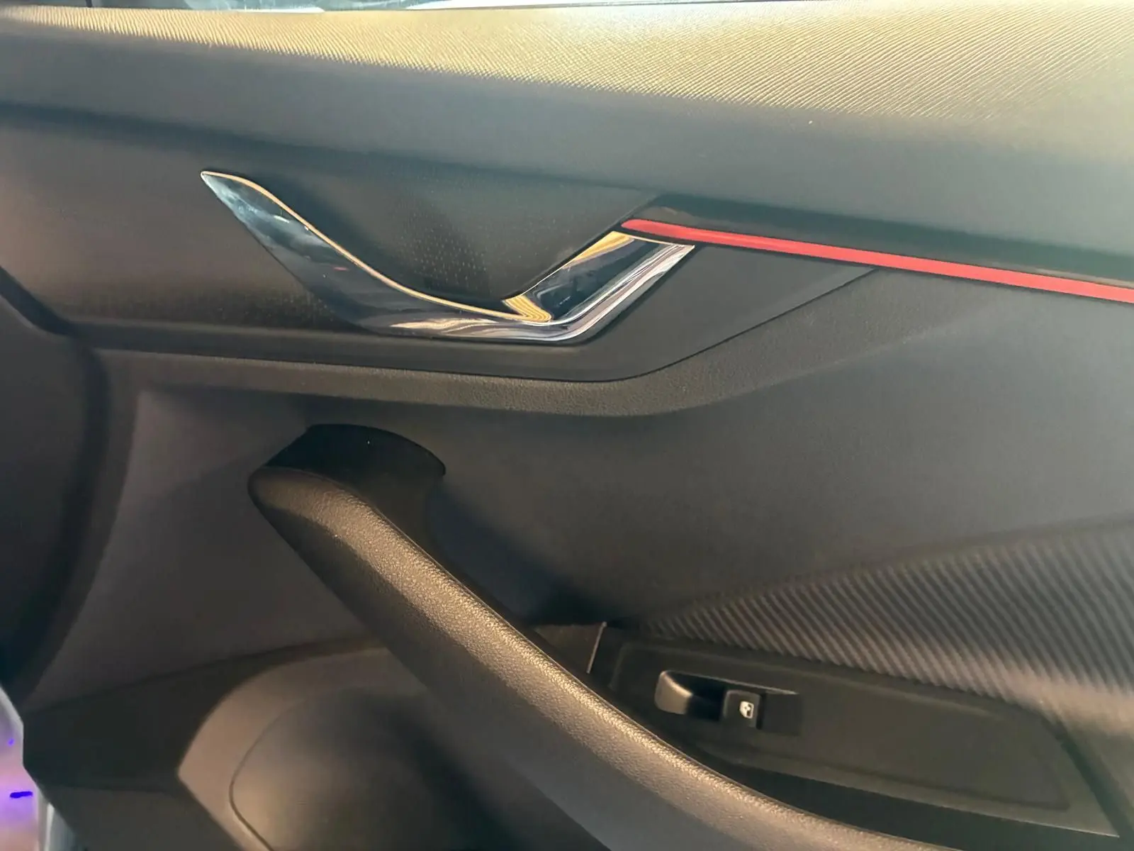 Détail de la poignée intérieure côté conducteur du Skoda Kamiq 2024 gris foncé avec insert rouge et finition carbone.