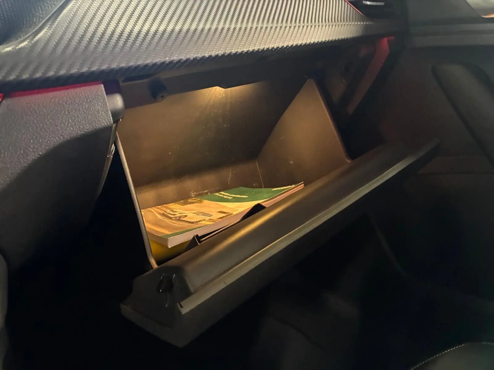 Intérieur du SKODA KAMIQ 2024 gris foncé, vue sur la boîte à gants ouverte avec éclairage intérieur et documents visibles.