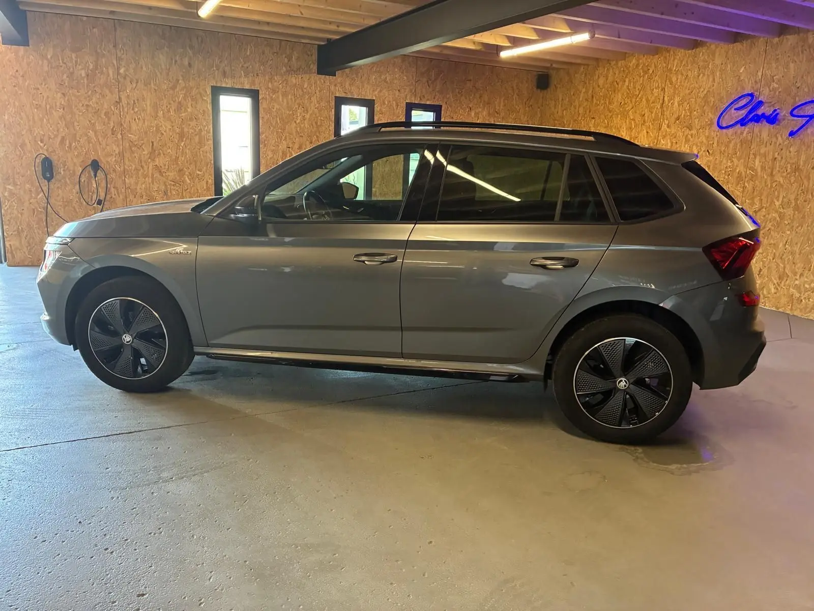 Vue de profil côté gauche d'un Skoda Kamiq gris foncé 2024 en version Monte-Carlo, stationné en intérieur.
