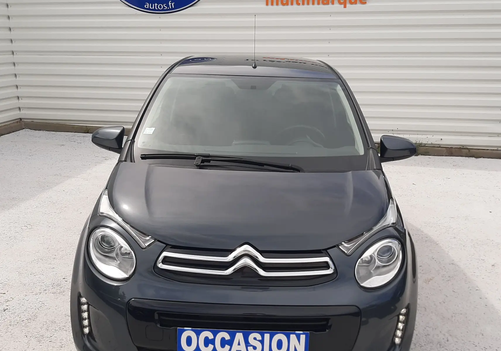Vue avant d'une Citroën C1 gris foncé 2019 avec phares ronds et logo double chevron bien visible.