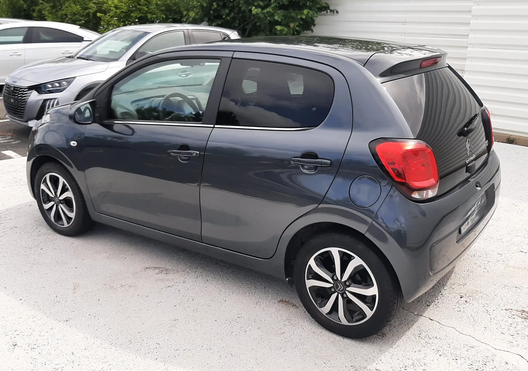 Citroën C1 gris foncé vue 3/4 arrière droit, compacte 5 portes avec jantes alliage bicolores et feux arrière rouges.