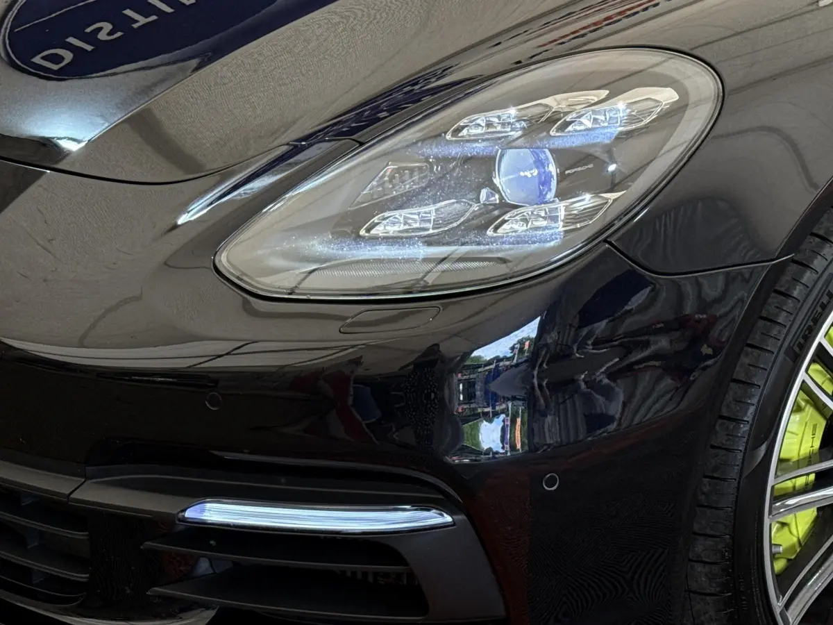 Gros plan sur l'avant droit noir brillant d'une Porsche Panamera 4 E-Hybrid Sport Turismo, avec phares LED et jante verte.