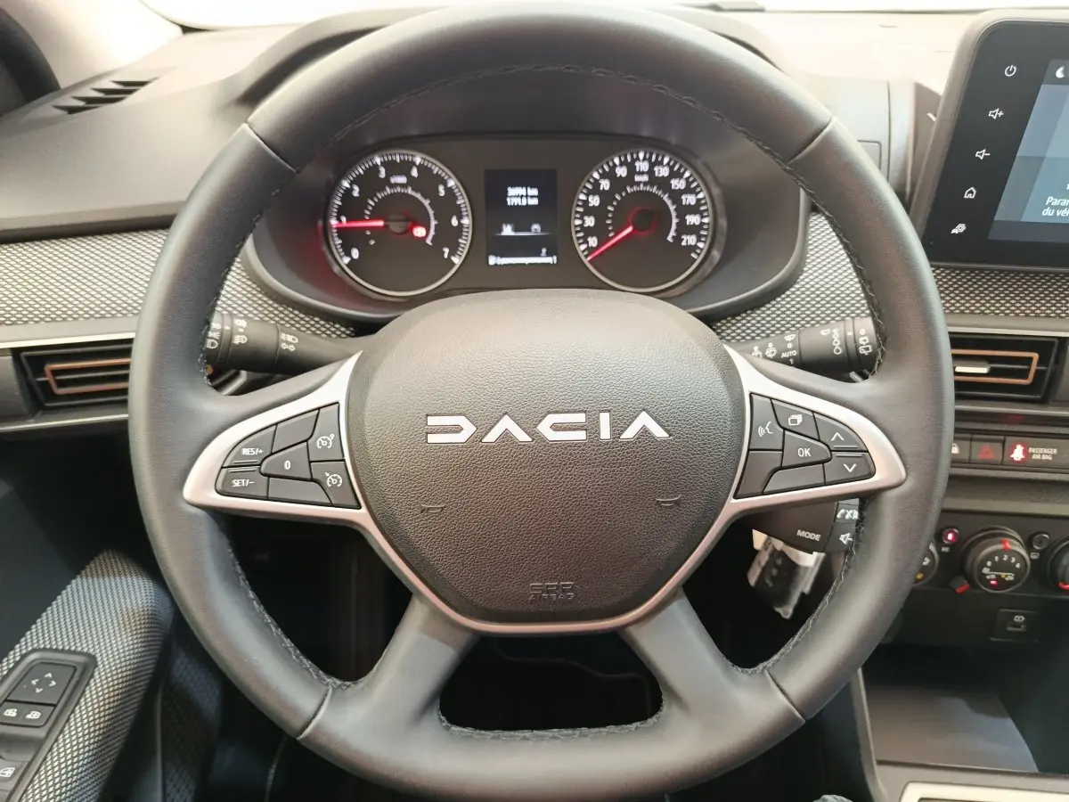 Vue rapprochée du volant cuir multifonctions noir de la Dacia Sandero 2023 avec tableau de bord et écran tactile visibles.