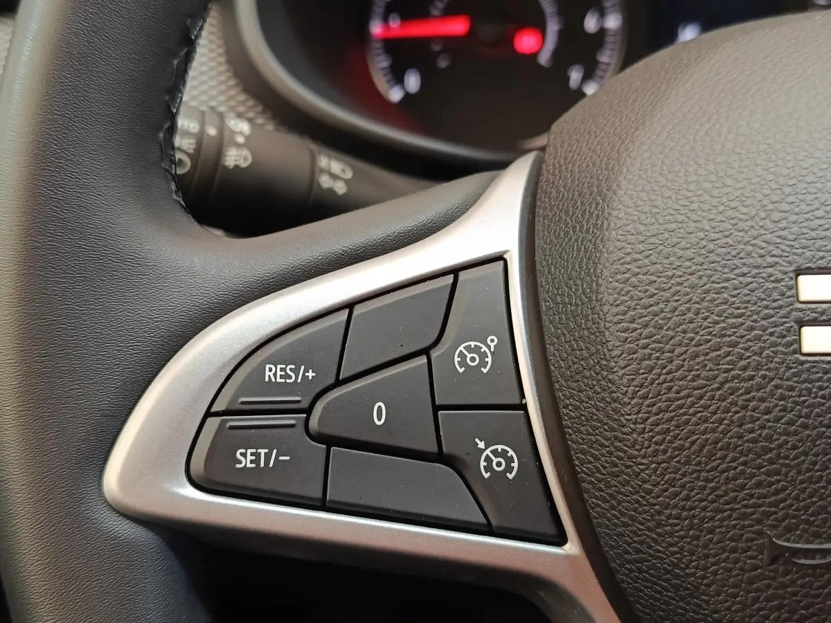 Gros plan sur le volant cuir synthétique gris d'une Dacia Sandero 2023, avec commandes du régulateur de vitesse visibles.