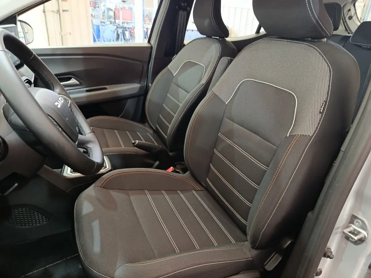 Vue intérieure côté conducteur de la Dacia Sandero Expression EGO-G 100 2023, sièges tissu noir avec surpiqûres contrastées.