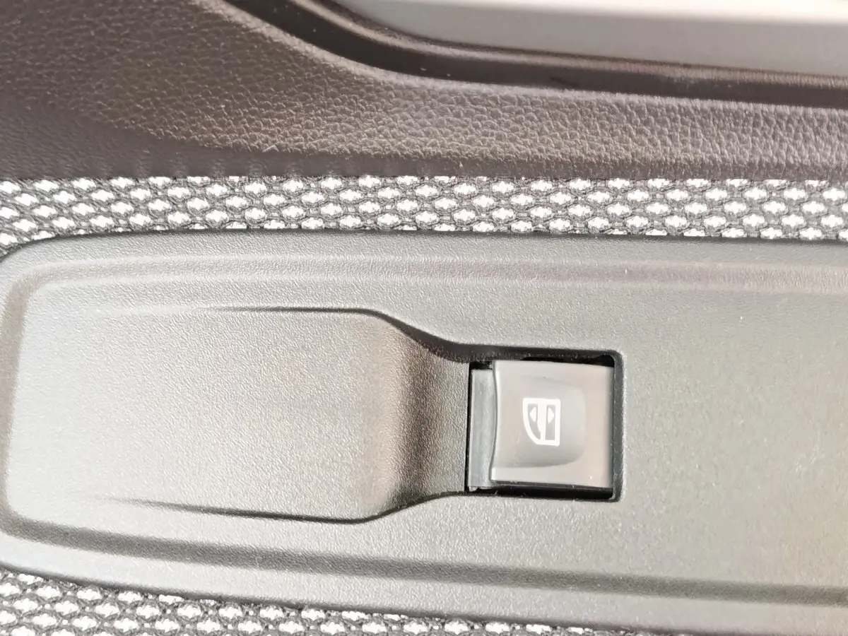 Gros plan sur l'interrupteur de lève-vitre côté porte intérieure d'une Dacia Sandero gris clair 2023.