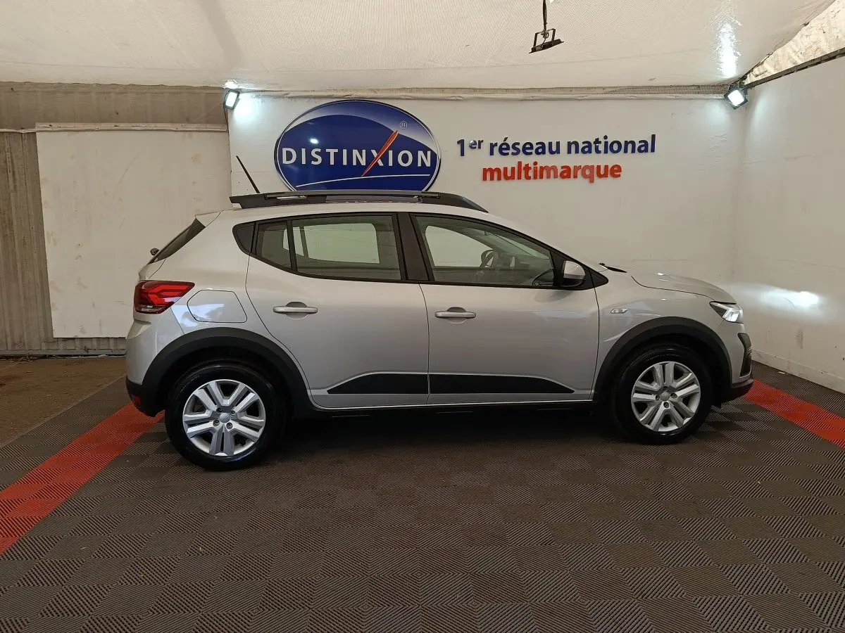 Vue de profil côté gauche d'une Dacia Sandero gris clair 2023 avec protections noires et jantes alliage.