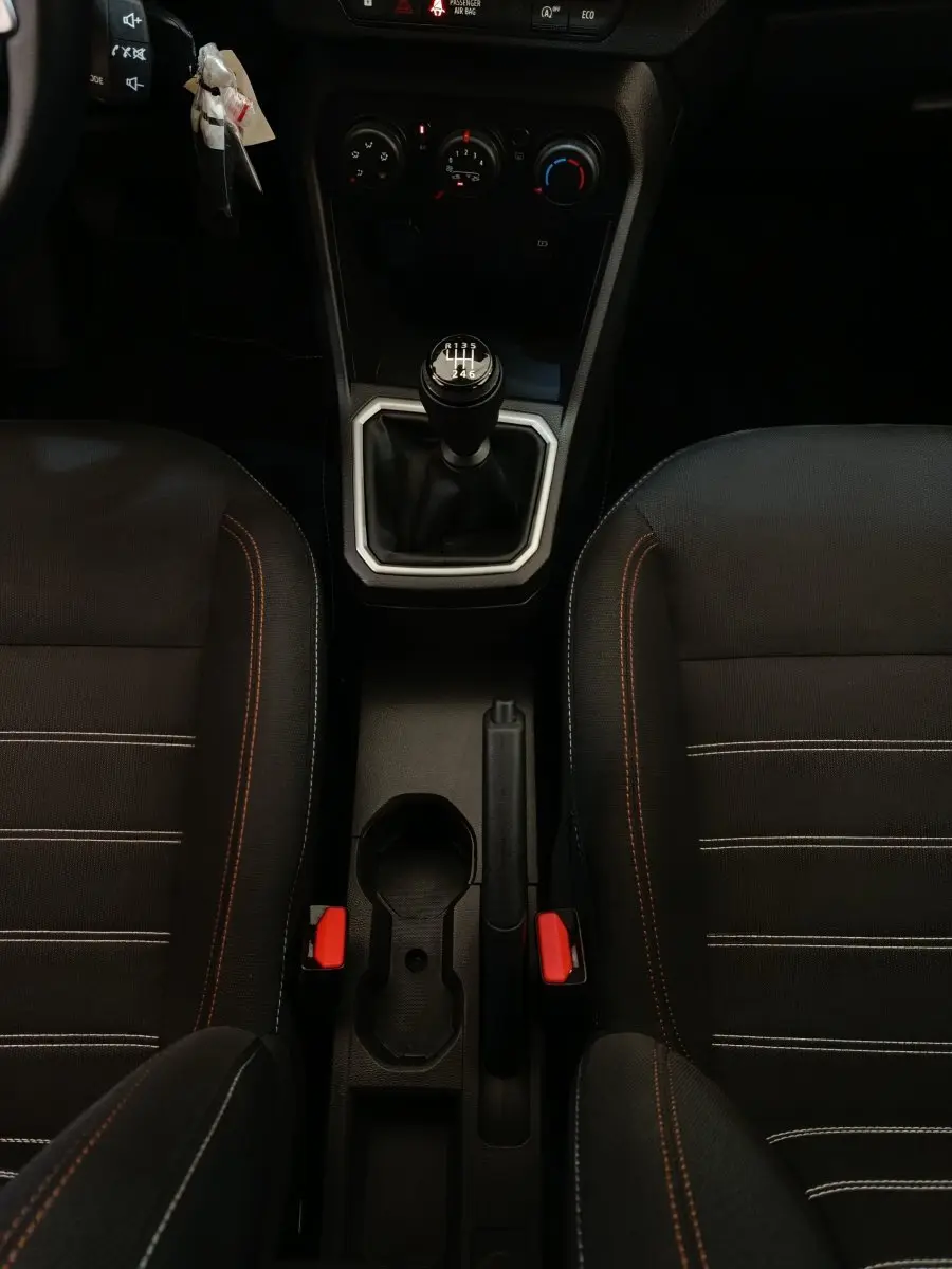 Vue plongeante sur la console centrale intérieure de la Dacia Sandero gris clair, avec levier de vitesse manuel et sièges noirs à surpiqûres orange.