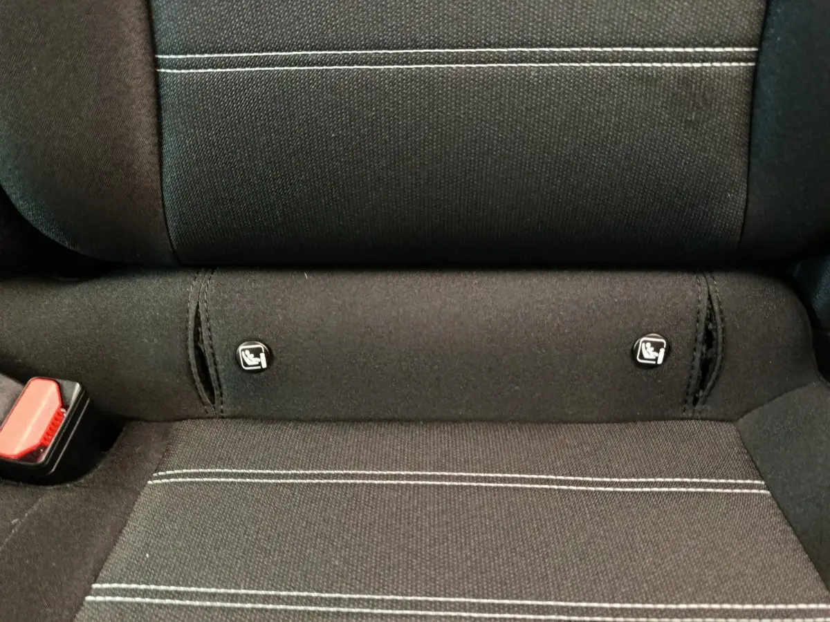 Gros plan sur la banquette arrière noire avec surpiqûres blanches et fixations Isofix visibles dans une Dacia Sandero gris clair.