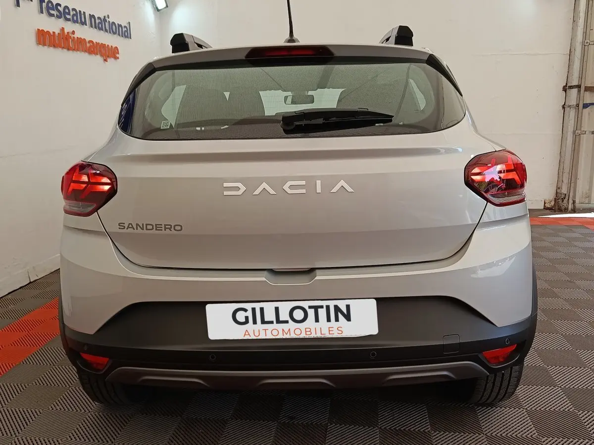 Vue arrière d'une Dacia Sandero gris clair 2023 avec feux LED et logo DACIA bien visible.