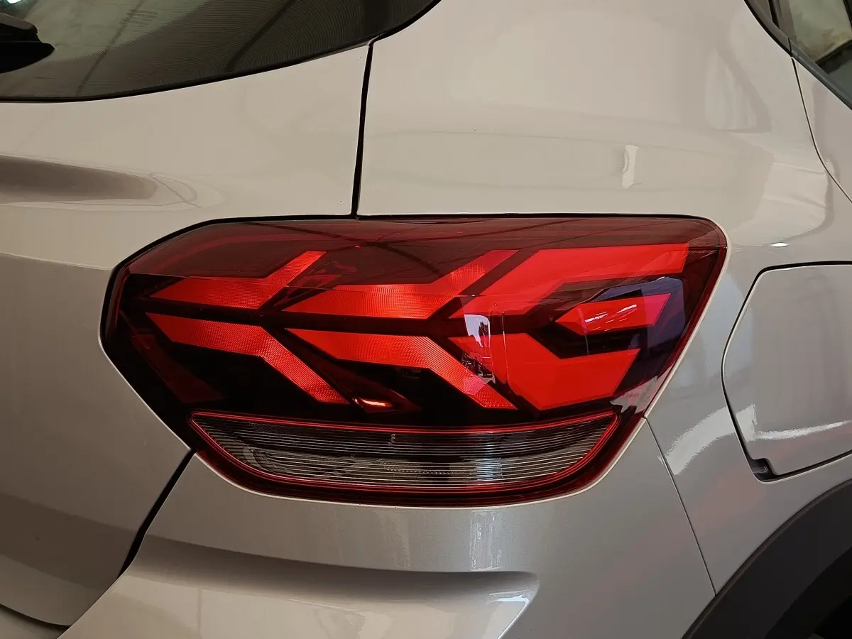 Gros plan sur le feu arrière droit rouge d’une Dacia Sandero gris clair 2023, avec la trappe à carburant visible.