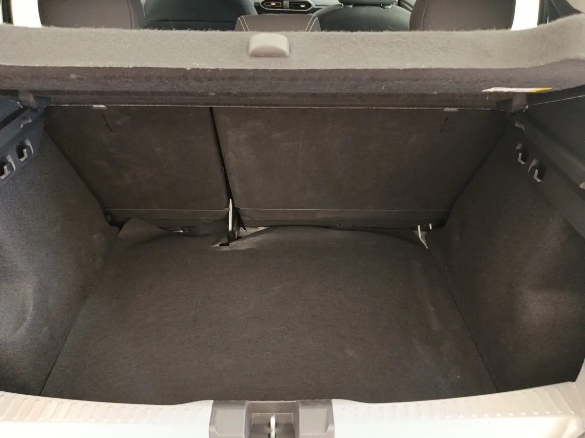 Coffre ouvert vu de l'arrière d'une Dacia Sandero gris clair 2023, montrant l'espace de chargement avec banquette rabattue.