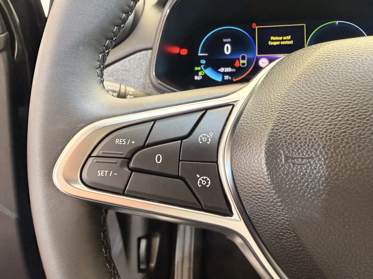 Gros plan sur le volant cuir synthétique noir de la Renault ZOE 2024 avec commandes multifonctions et tableau de bord digital.
