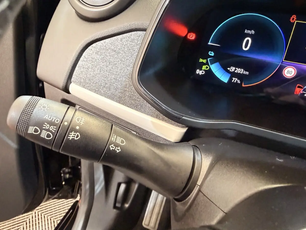 Gros plan sur la manette de commande des phares et clignotants à gauche du tableau de bord numérique bleu de la Renault ZOE noire.