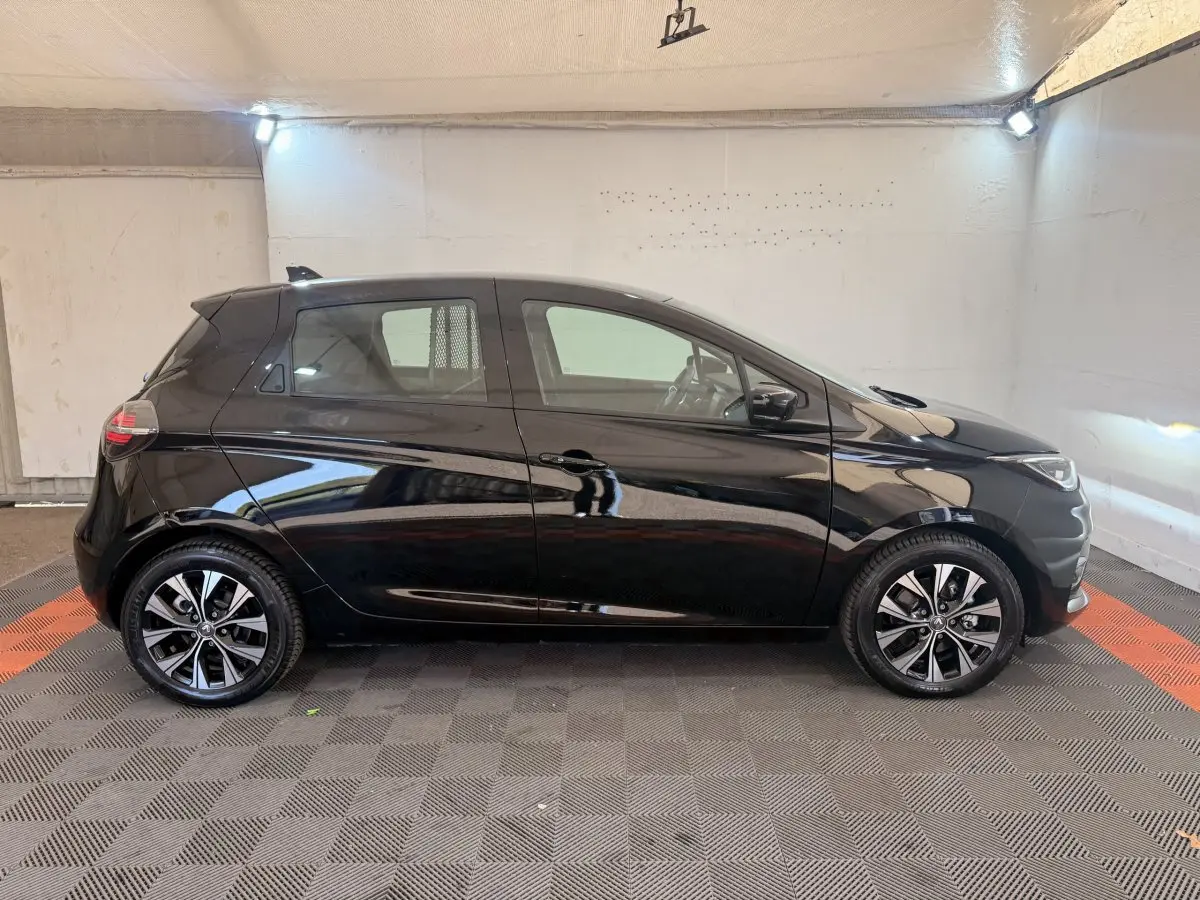 Profil droit d'une Renault ZOE noire 2024 avec jantes alliage distinctives dans un garage éclairé.