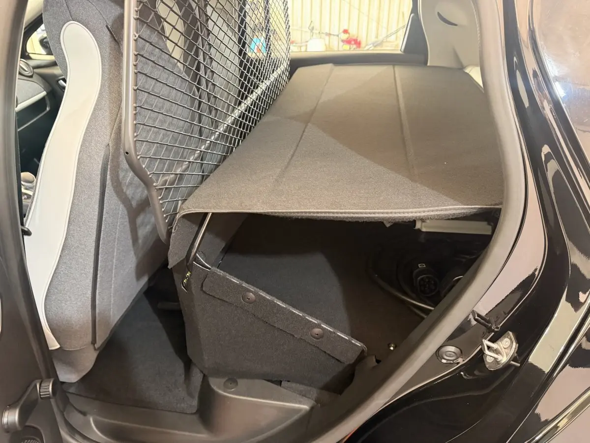 Vue intérieure côté droit du coffre ouvert de la Renault ZOE noire 2024 avec filet de séparation et câble de charge visible.