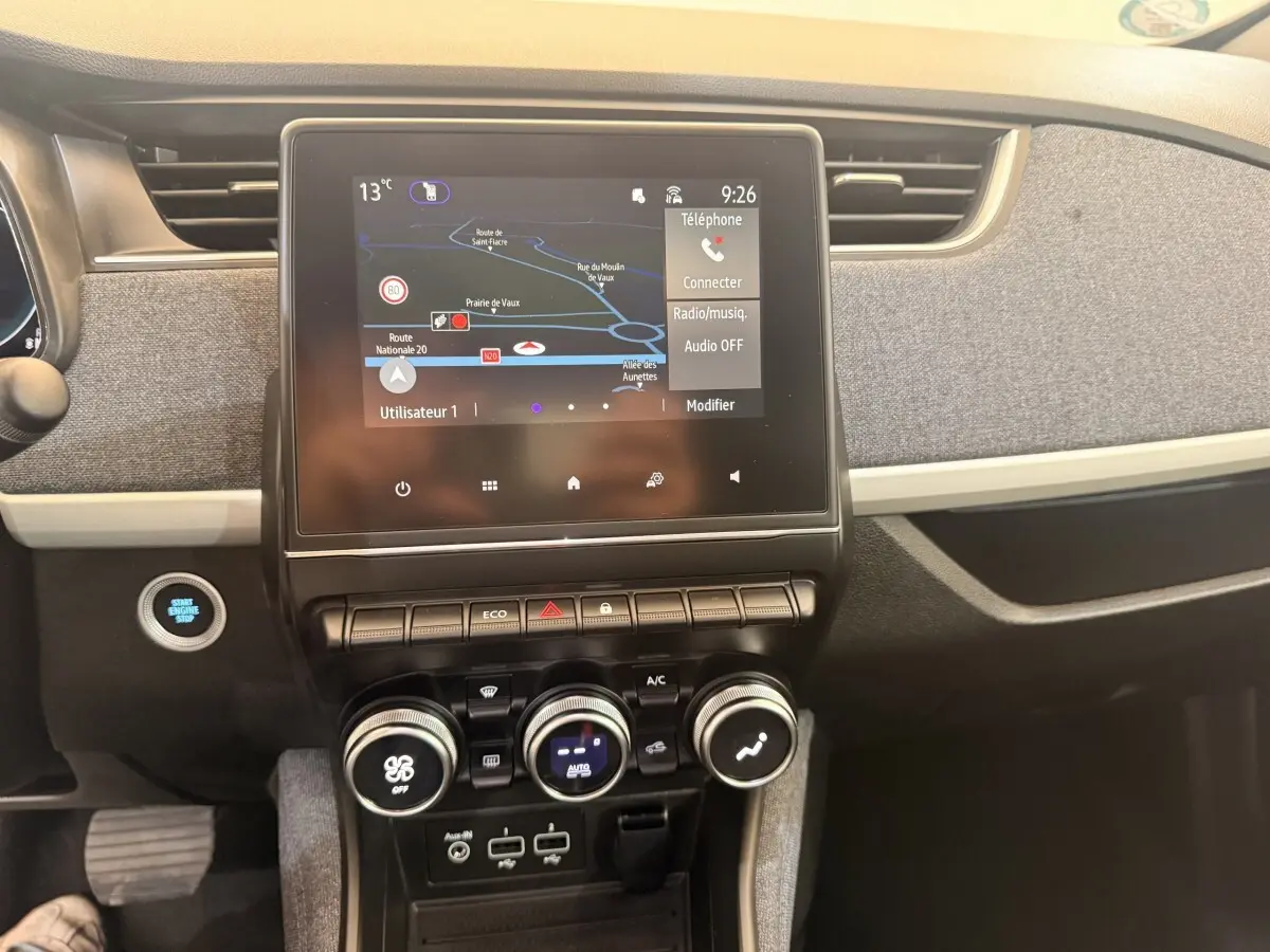 Vue intérieure centrée sur l’écran tactile et la console de la Renault ZOE noire, avec commandes climatisation et bouton démarrage.