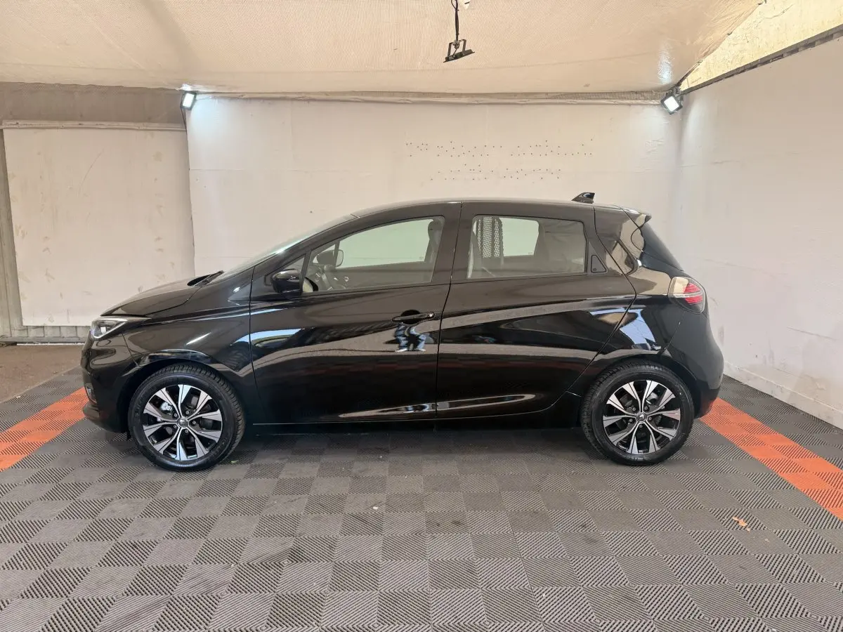 Renault ZOE noire vue de profil côté gauche, avec jantes alliage et lignes fluides, en intérieur éclairé.