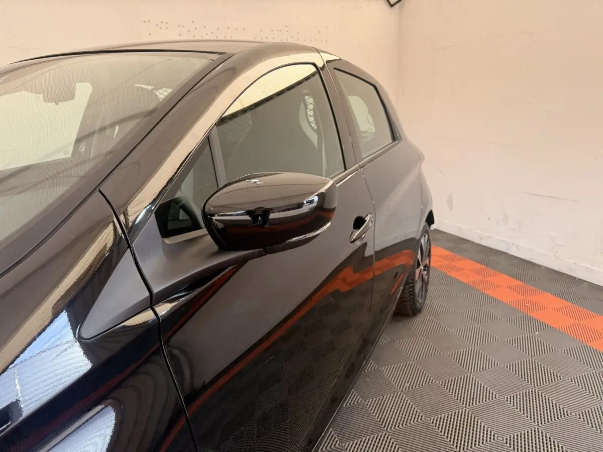 Vue de profil côté gauche sur une Renault ZOE noire électrique, mettant en valeur la portière et le rétroviseur.