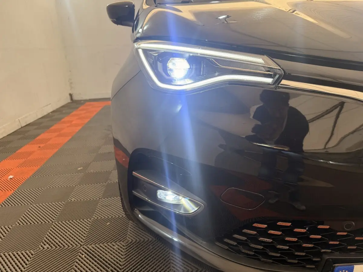 Gros plan sur l'avant droit noir de la Renault ZOE 2024 avec phares LED allumés et calandre visible.