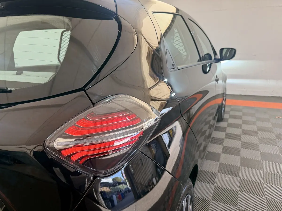 Vue 3/4 arrière droite d'une Renault ZOE noire 2024 avec feux arrière LED distinctifs dans un parking couvert.