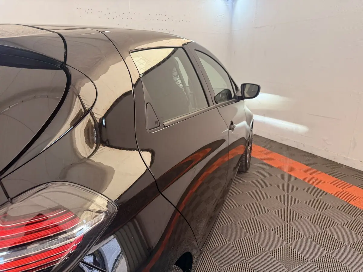 Vue arrière côté droit d'une Renault ZOE noire garée sur un sol à damiers gris et orange, avec feux arrière visibles.