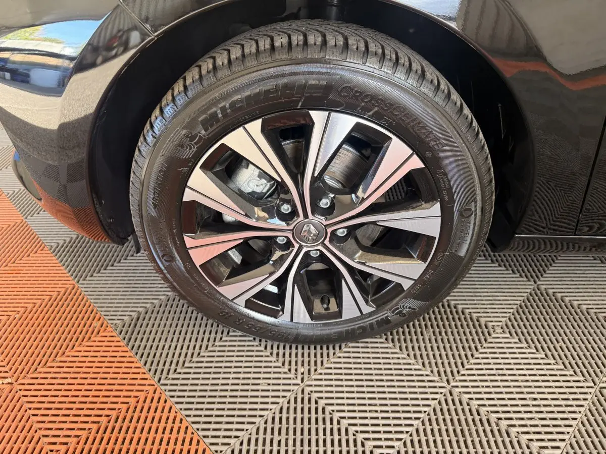 Gros plan sur la roue avant droite noire d'une Renault ZOE 2024 avec jante alliage bicolore et logo central Renault.